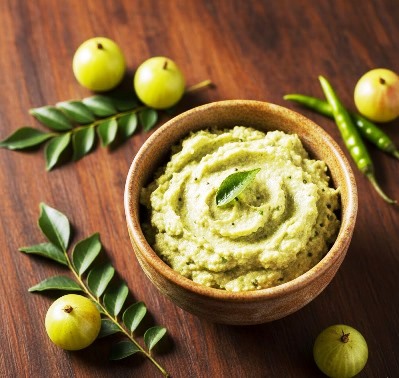 Homemade amla chutney prepared with gooseberries, coconut, and curry leaves and served in a bowl surrounding full gooseberries, green chillies and curry leaves